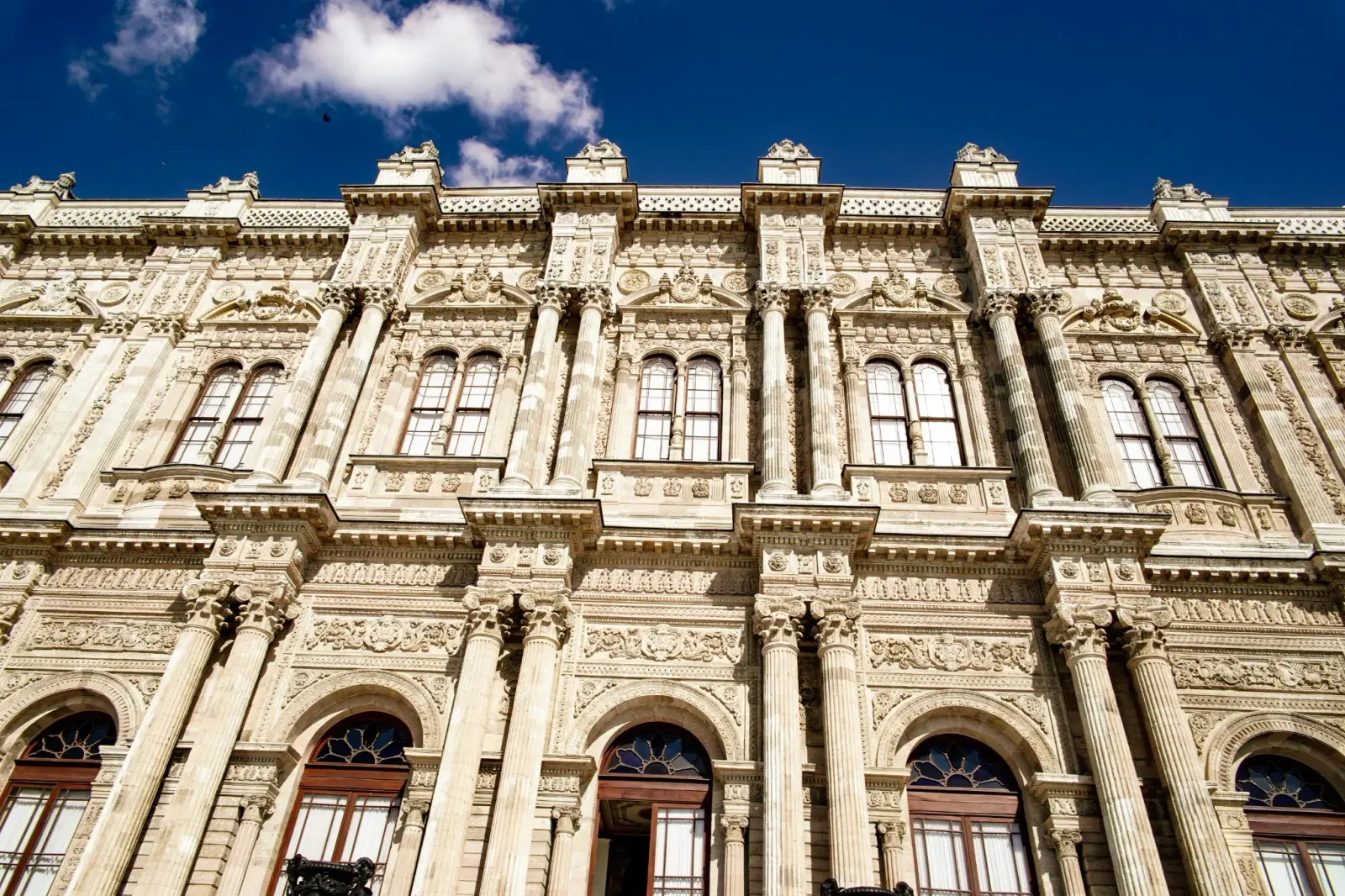 The richly carved stone facade of Dolmabahçe Palace, seen from below against a blue sky.